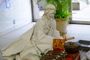 白い女神の彫刻に扮した人物が楽しそうで打楽器を叩いている。